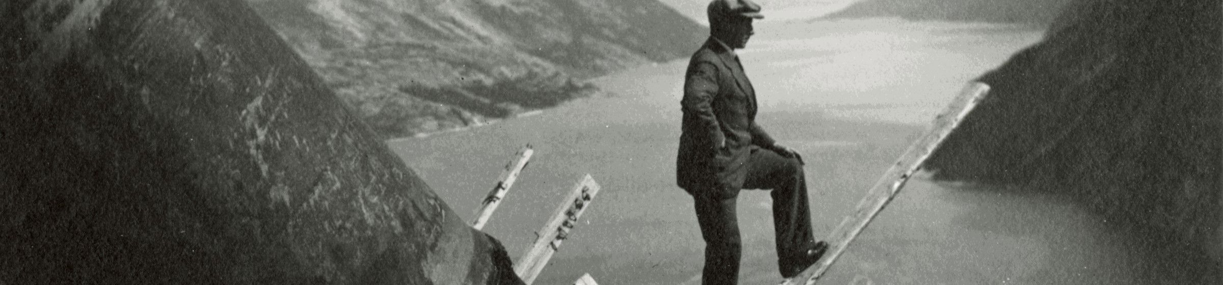 Black and white image of man looking out over a fjord